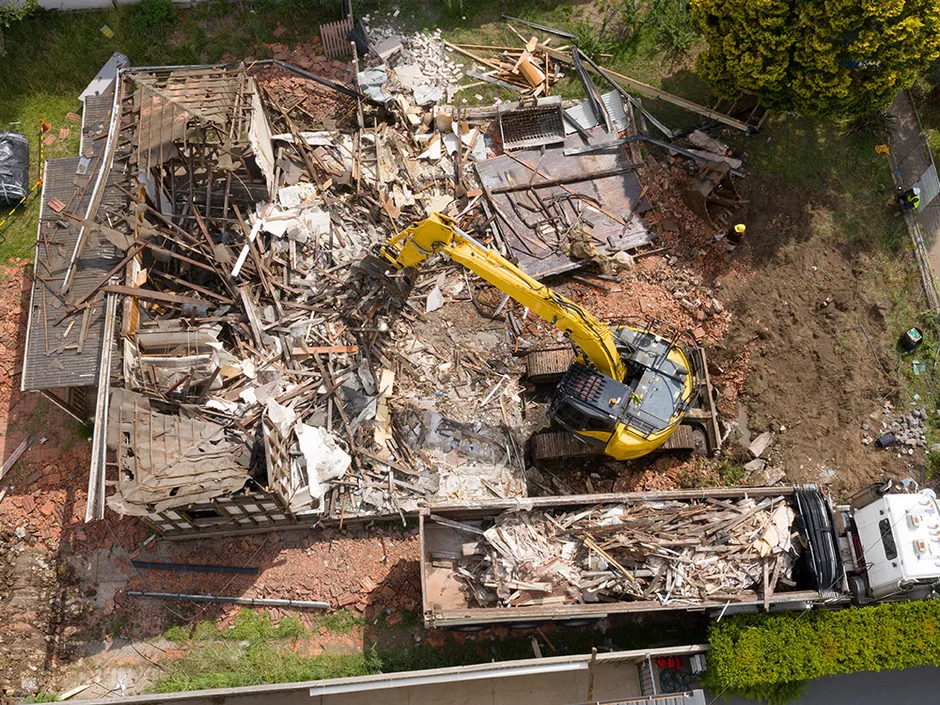 Aerial view of a torn down house with an excavator loading the debris into a dump truck, debris removal