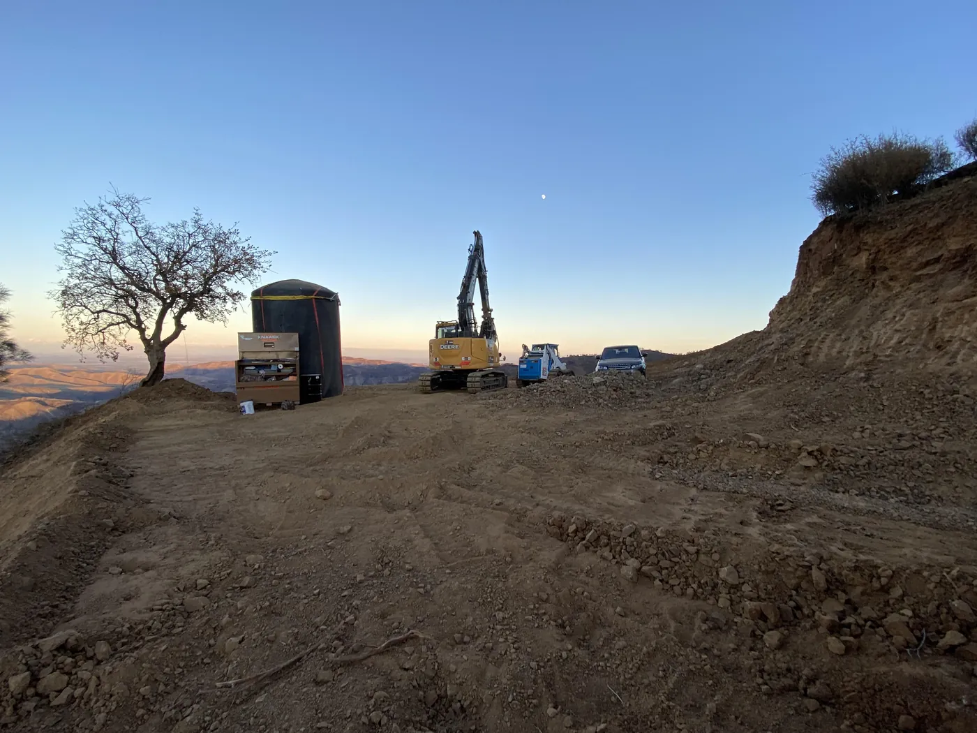 Excavator on a building pad cut into a hillside at sunrise, excavation