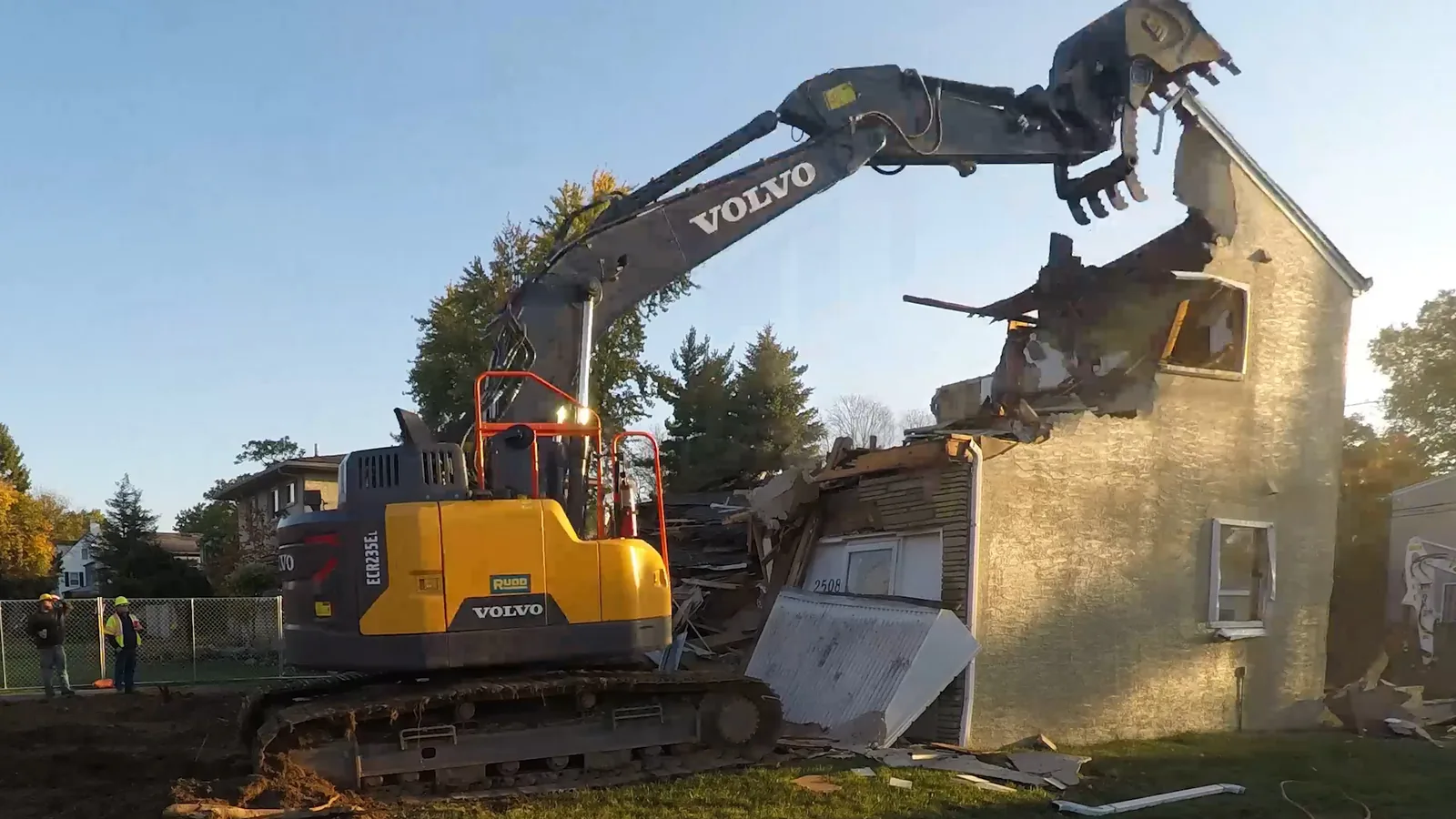 Excavator with a demolition grapple tearing down the upper floor of a two story house, demolition contractor