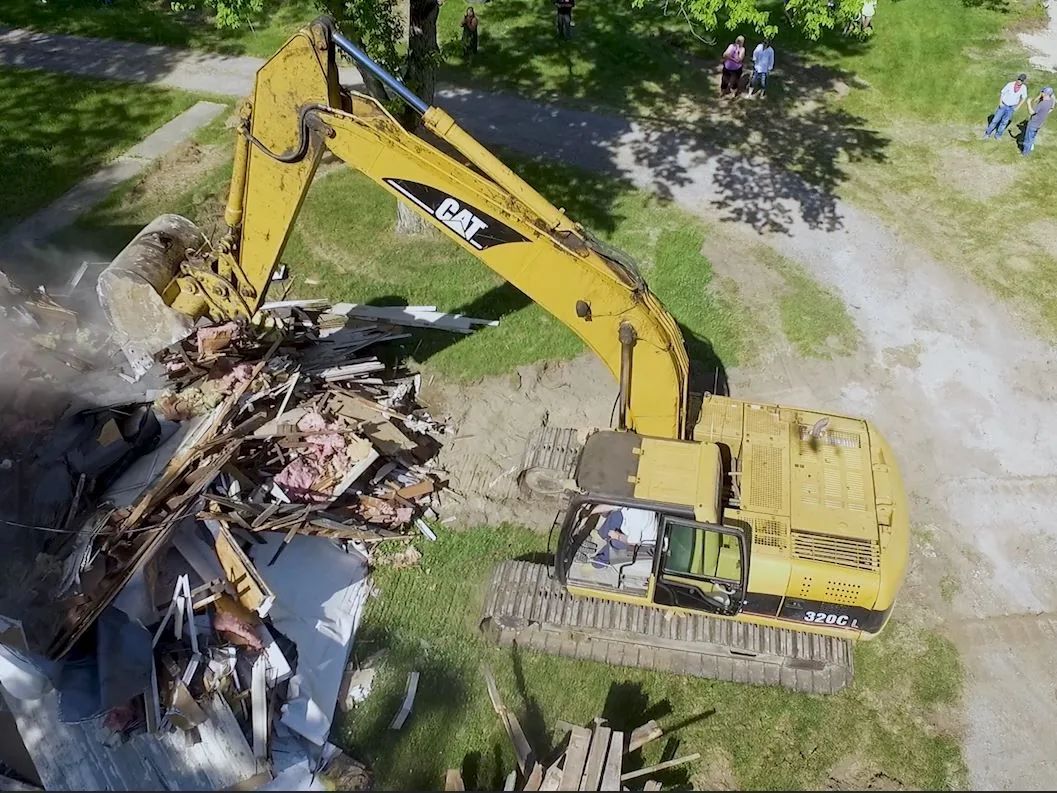 Aerial view of an excavator tearing down an old house into a pile of framing and insulation, house demolition