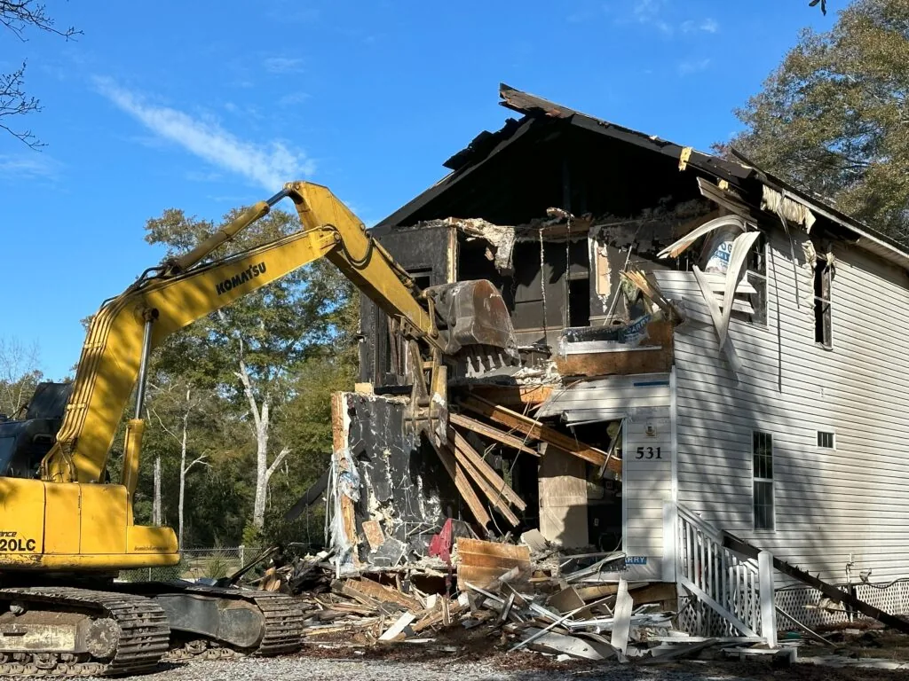 Excavator tearing into the side of a two story vinyl sided house, house demolition
