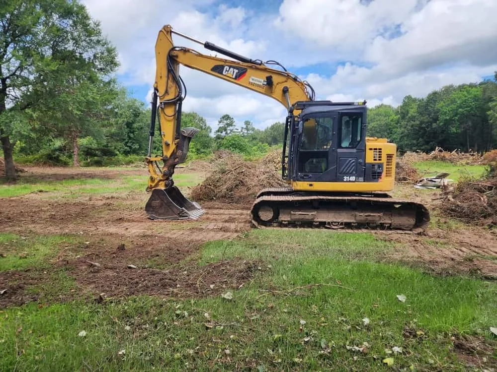 Excavator on a cleared lot with brush piles pushed up behind it, land clearing