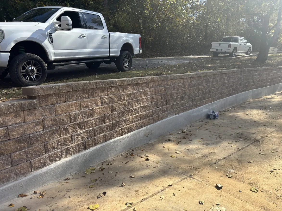 Finished tan block retaining wall holding up a driveway with two pickup trucks parked above, retaining walls