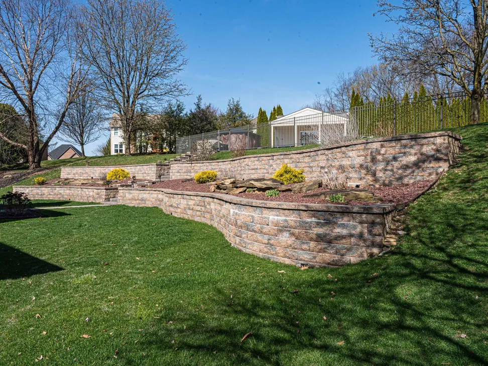 Tiered tan block retaining walls with planting beds stepping up a lawn, retaining walls