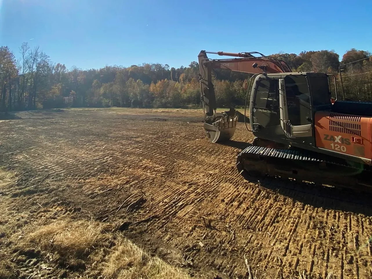 Excavator beside a freshly rough graded open lot with fall woods behind, site development